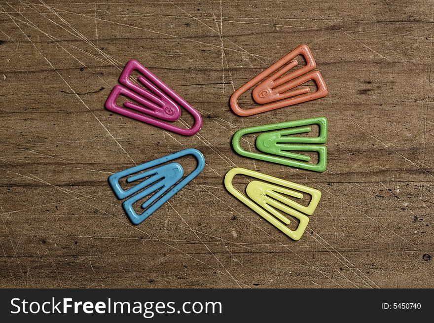 Color paper clips on wooden table.