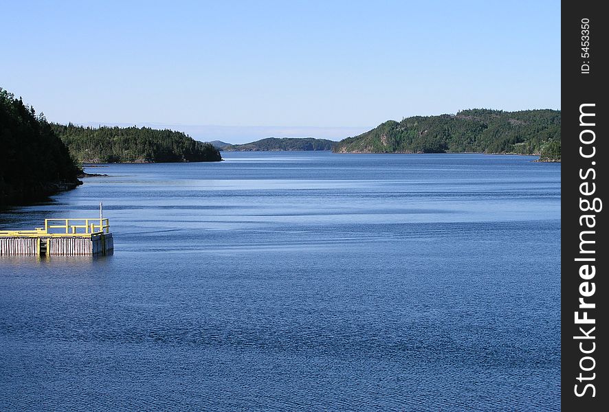 Coastal scene with bright blue waters, sky, and sunny green forest on the sides. Coastal scene with bright blue waters, sky, and sunny green forest on the sides.