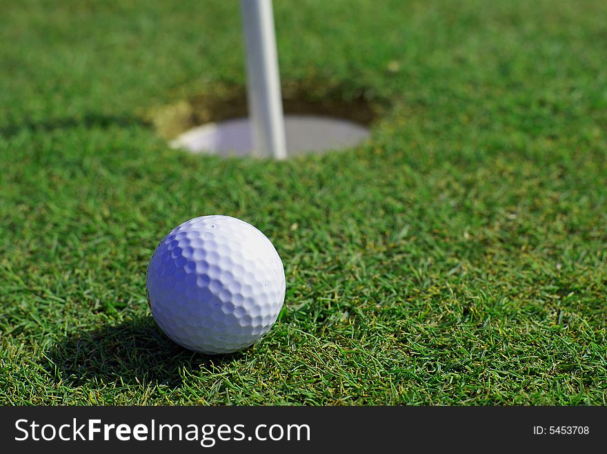Golfball in front of the green grass hole. Golfball in front of the green grass hole