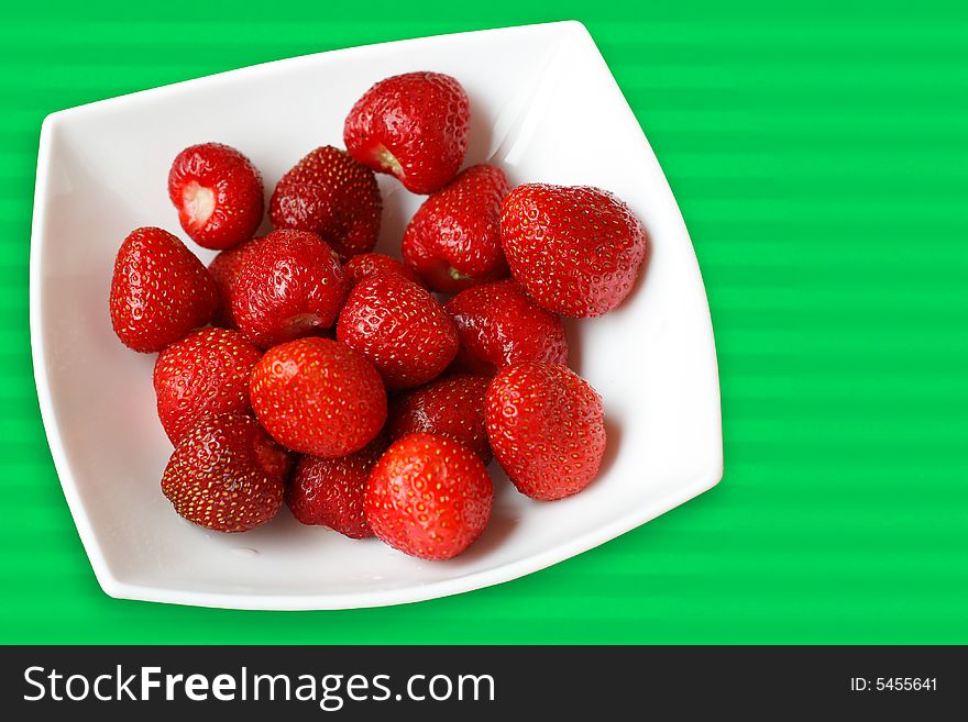 Fresh strawberries in white bowl on green back