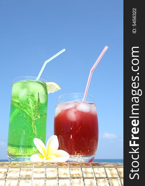 Green drink in long glass with estragon and red drink with icecubes standing on the gold. Green drink in long glass with estragon and red drink with icecubes standing on the gold