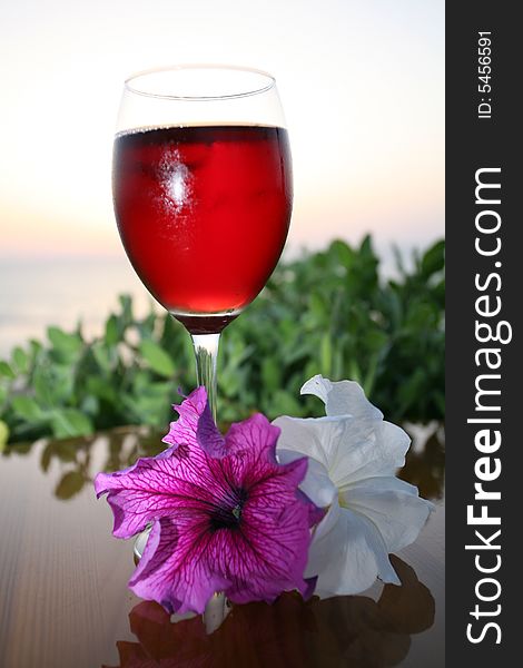 Glass of red wine with two beautiful flowers on the wood table