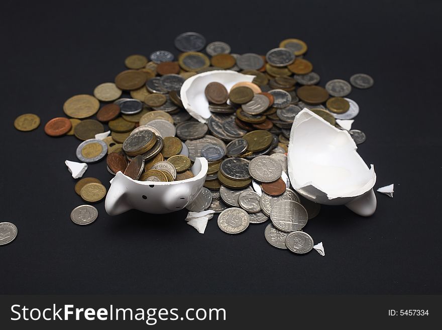 A broken piggy bank isolated on a dark background with loads of coins from around the world.