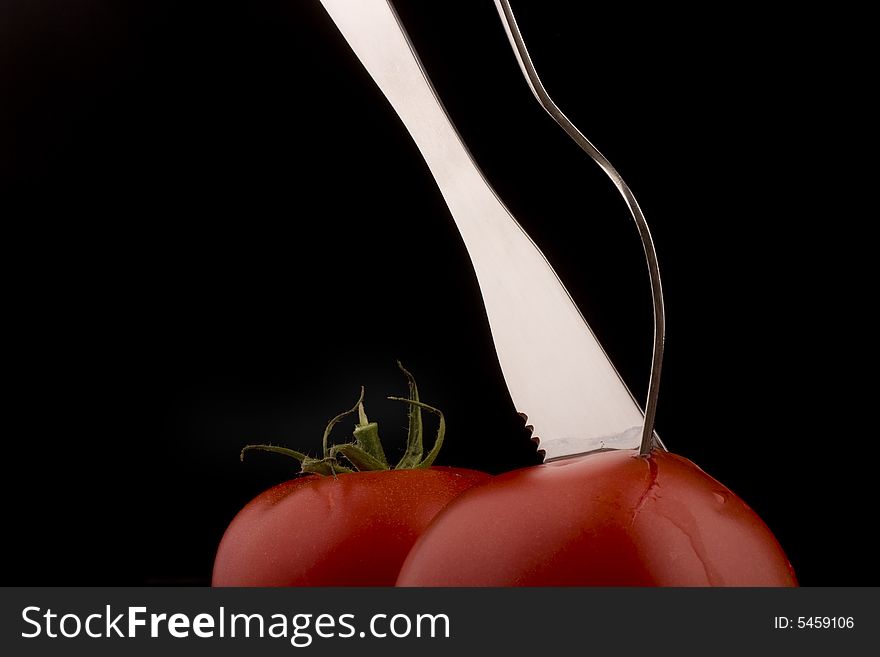 Knife with forks help slices juicy  tomato. Other tomato in background still uncut. Knife with forks help slices juicy  tomato. Other tomato in background still uncut.