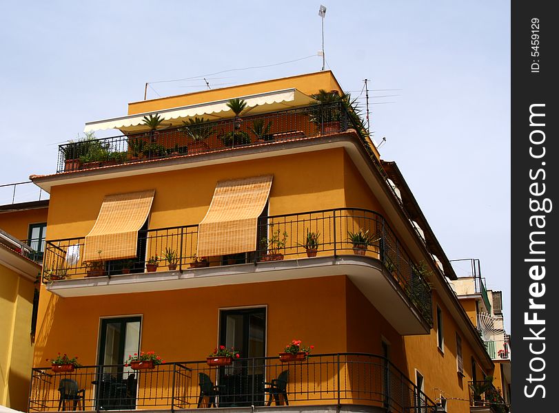 Goldenrod building with balconies and potted flowers in Italy. Goldenrod building with balconies and potted flowers in Italy.