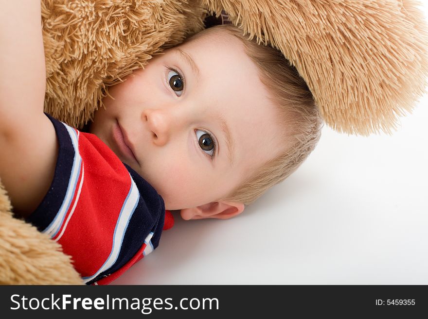 Little boy lye on white bed and embrace toy bear