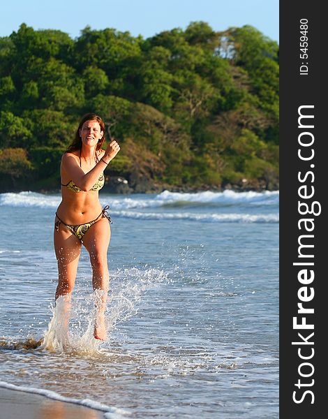 A young woman at the beach in the water. Jumping for joy with a bikini. Ideal summer / vaction shot. A young woman at the beach in the water. Jumping for joy with a bikini. Ideal summer / vaction shot.