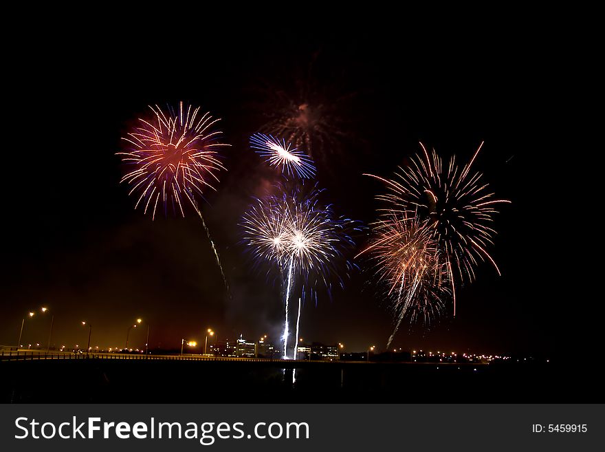 Fireworks display viewed at night exploding over a bridge.