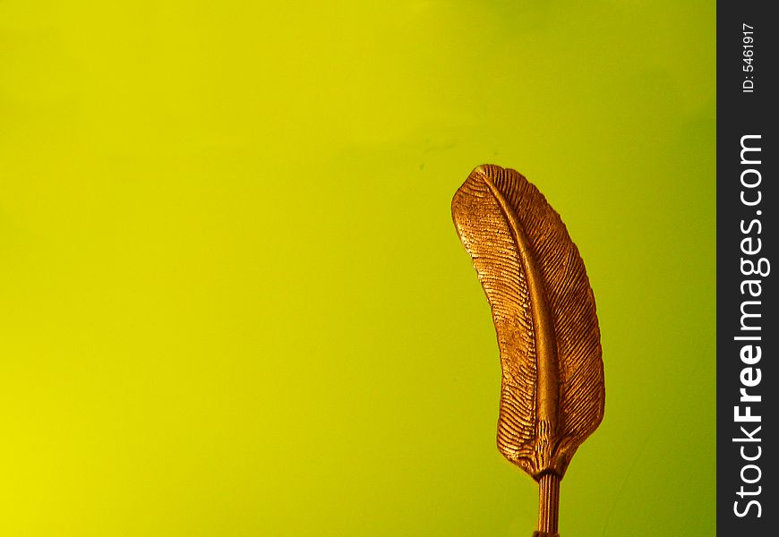 A bronze feather standing alone on a background of a brilliant apple green colored wall. A bronze feather standing alone on a background of a brilliant apple green colored wall