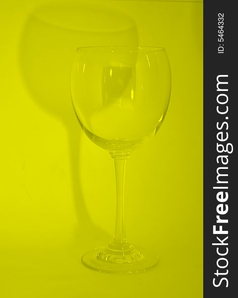 Single wine glass on yellow background with wine glass shadow