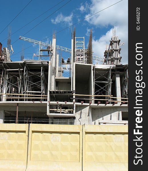 A building site, a hoisting crane and unfinished walls on the blue sky background.