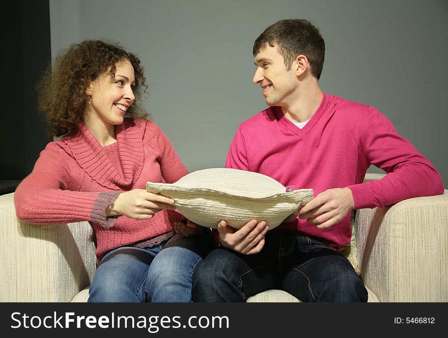 Couple sit on sofa with pillow and look at each other
