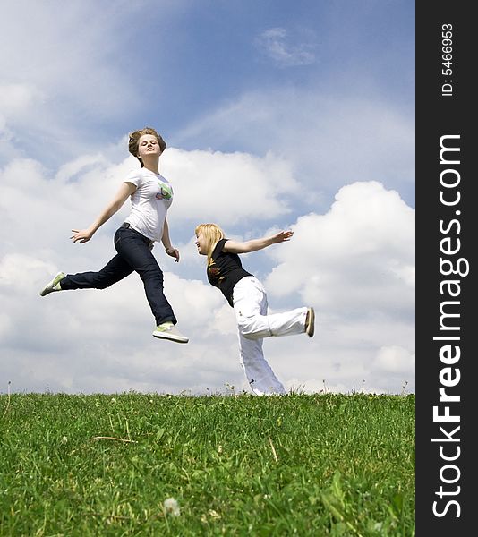 The two happy jumping girls on a background of the blue sky