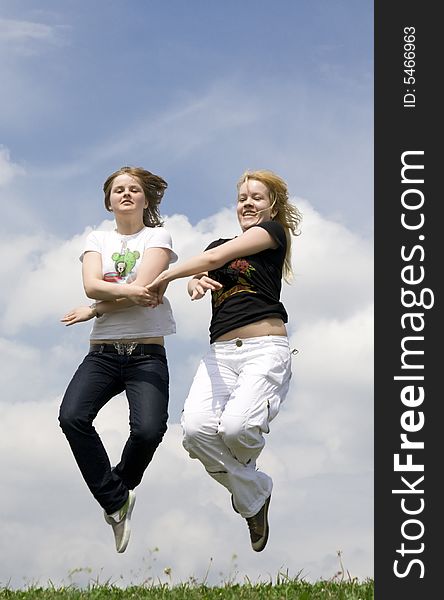 The two happy jumping girls on a background of the blue sky