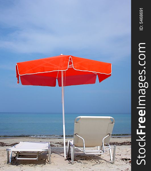 Two lounge chairs under a red umbrella on the sandy beach. Two lounge chairs under a red umbrella on the sandy beach