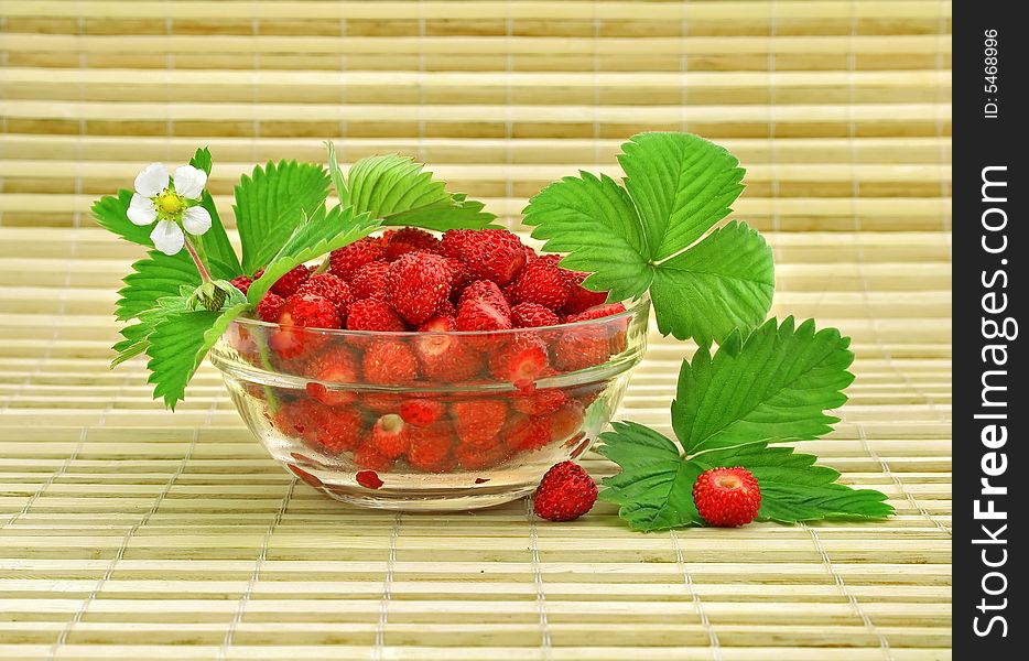 Red strawberry fruits with green leafs and flower in glass vase