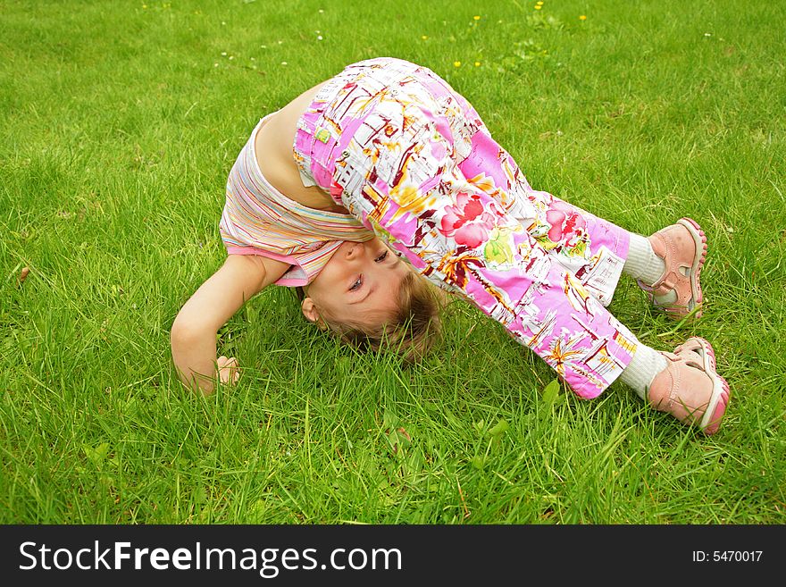 A little girl makes exercise on grass