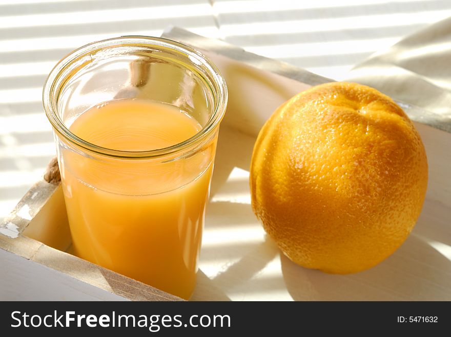 Orange juice and one orange on a tray