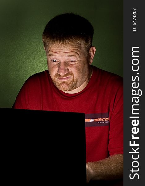 A man looking at a Notebook computer looking tired. A man looking at a Notebook computer looking tired