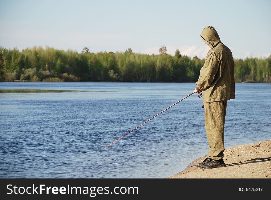 Fisherman on the river beach with fishing-rod