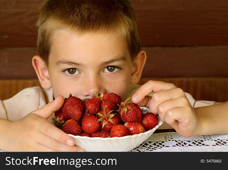 The boy of eight years sits at the table with the basin the strawberries. The boy of eight years sits at the table with the basin the strawberries
