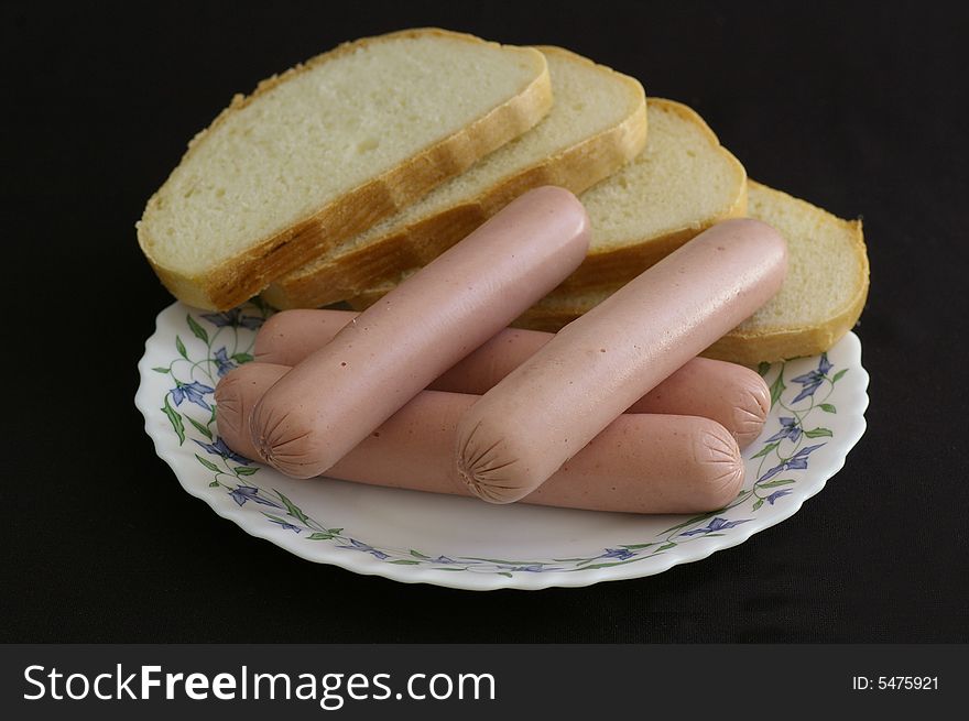 Several sausages with the slices of bread against the black background. Several sausages with the slices of bread against the black background