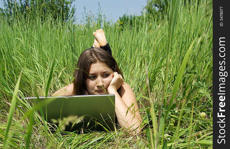 The girl works on a computer on a green grass. The girl works on a computer on a green grass