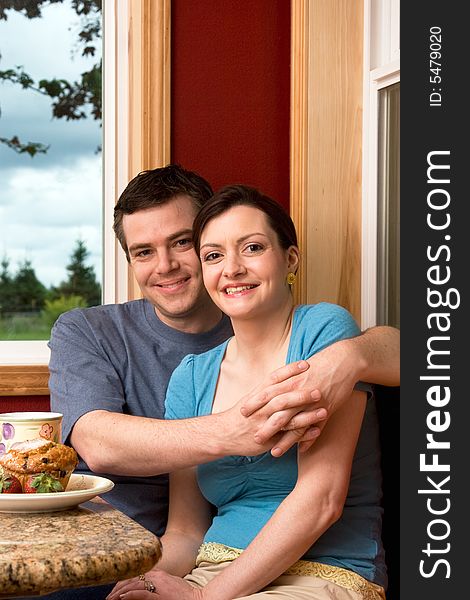 An attractive couple smiling over breakfast.  The man is hugging the woman.  Vertically framed shot. An attractive couple smiling over breakfast.  The man is hugging the woman.  Vertically framed shot.