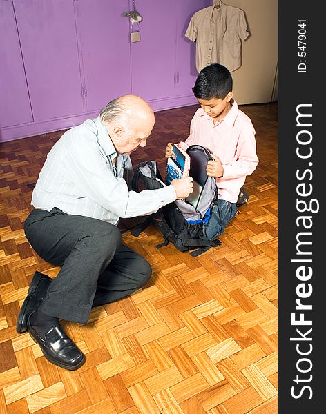 Grandfather is teaching the grandson how to pack his bag. Grandson is patiently taking instructions from grandfather. This is vertically framed. Grandfather is teaching the grandson how to pack his bag. Grandson is patiently taking instructions from grandfather. This is vertically framed.