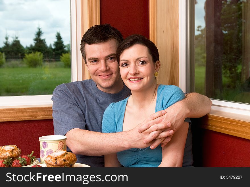 A couple smiling by large windows at home.  The man is hugging the woman.  Horizontally framed shot. A couple smiling by large windows at home.  The man is hugging the woman.  Horizontally framed shot.