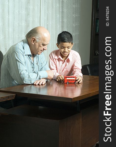 Grandfather and Grandson are seated at a table looking at a red double decker bus. Vertically framed photograph. Grandfather and Grandson are seated at a table looking at a red double decker bus. Vertically framed photograph.