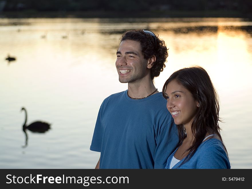 Couple smiling in front of a pond with swans swimming by. Horizontally framed photograph. Couple smiling in front of a pond with swans swimming by. Horizontally framed photograph