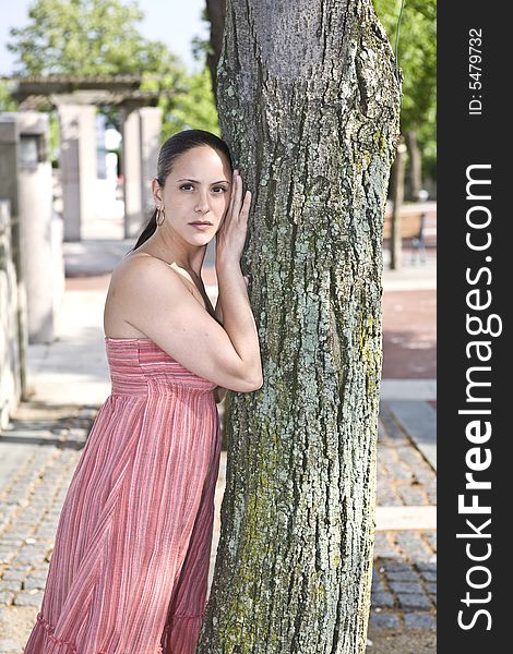 A beautiful young woman posing by a tree in a public park. A beautiful young woman posing by a tree in a public park