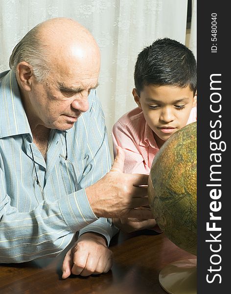 Grandfather and Grandson are seated at a table looking at a globe together. Vertically framed photograph. Grandfather and Grandson are seated at a table looking at a globe together. Vertically framed photograph.