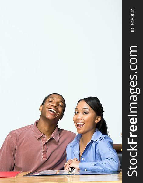 Two Teens are are seated at a desk laughing, and smiling. There are folders and paper on the desk. Vertically framed photograph. Two Teens are are seated at a desk laughing, and smiling. There are folders and paper on the desk. Vertically framed photograph