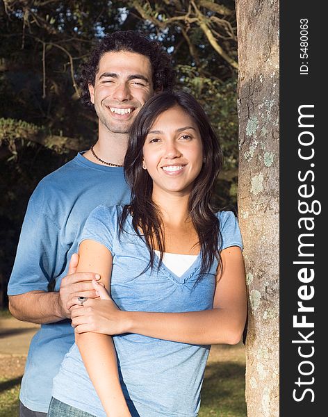 Happy couple hold each other and smile as they lean against a tree. Vertically framed photograph. Happy couple hold each other and smile as they lean against a tree. Vertically framed photograph