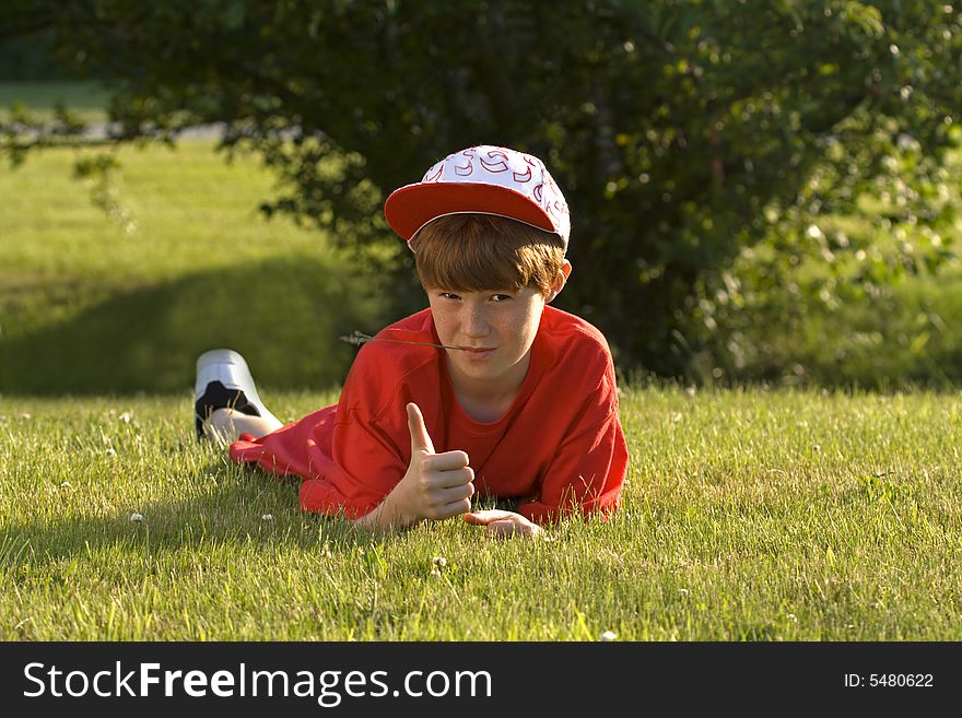 Boy in red t-shirt lies at green field