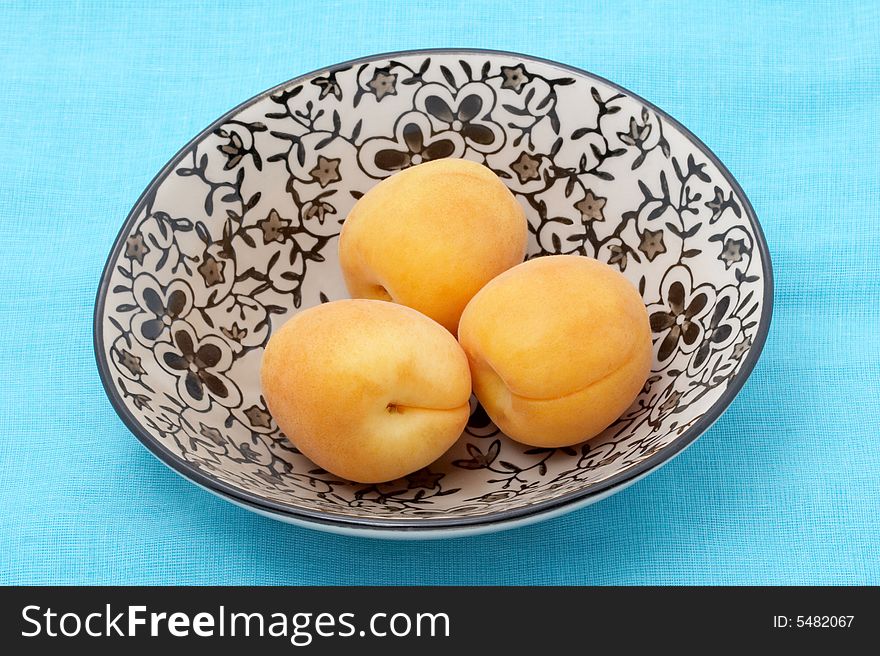 Three apricots in a bowl on blue fabric