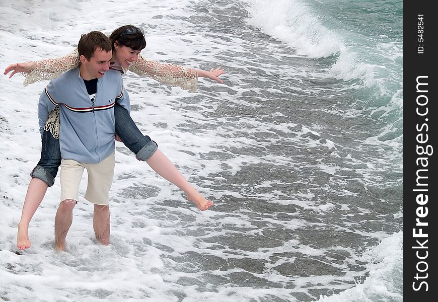 Funny young couple carrying piggyback on seashore