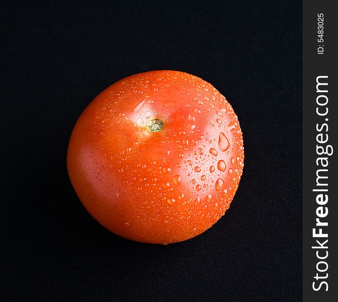 A single tomato with waterdrops on black fabric; isolated. A single tomato with waterdrops on black fabric; isolated.