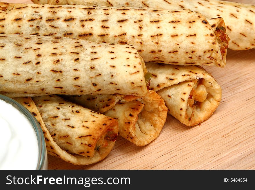 Stack of chicken taquitos with hot sauce and sour cream in kitchen or restaurant