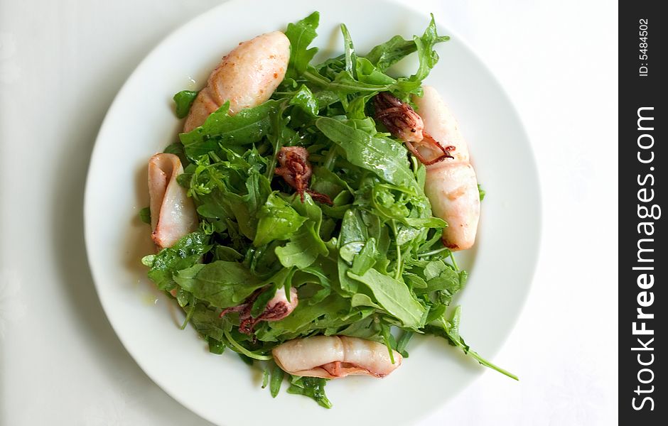 A roasted squids with rucola on a white plate. A roasted squids with rucola on a white plate.