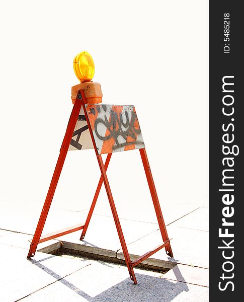 Orange reflector on a barricade covering an open pit on the sidewalk.