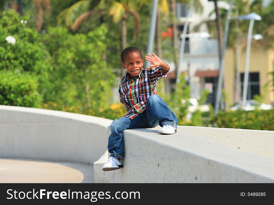 Young boy sitting on a concrete ledge and waiving. Young boy sitting on a concrete ledge and waiving.