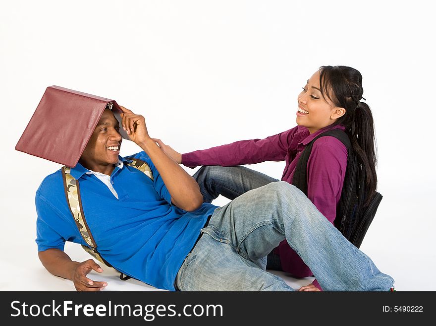 Studious, attractive teen couple flirting. The young man is lounging on the ground with a folder on his head. The young woman, who is sitting on the ground, is looking at him laughing.