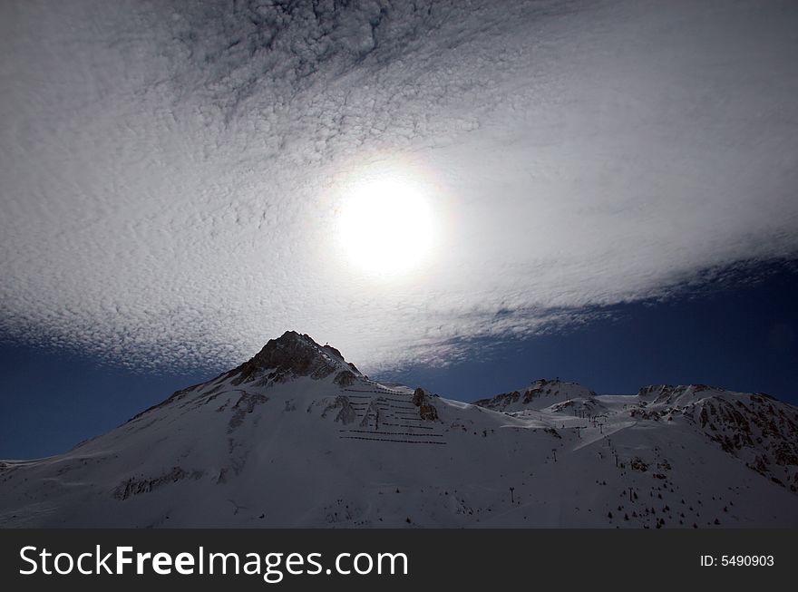 A sun behind dispersion of clouds, above picks of mountains. A sun behind dispersion of clouds, above picks of mountains