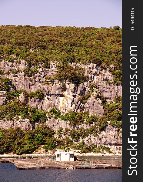 Rocks with in front a fish farm in the river