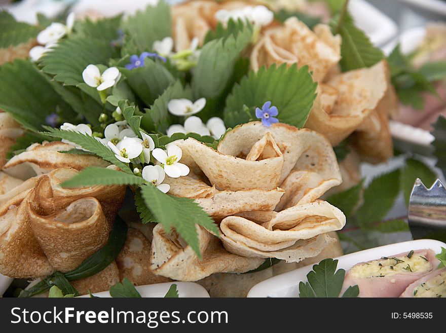 Stuffed and folded pancake is sitting on a plate, decorated with leaves and flowers