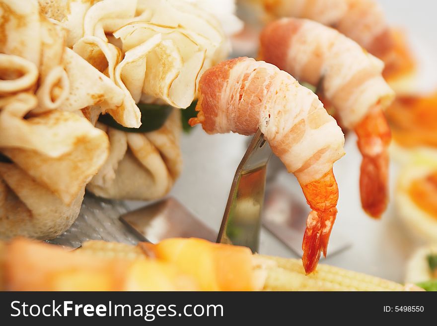 Prawns are wrapped in bacon and are sitting on serving table surrounded by stuffed pancakes. Prawns are wrapped in bacon and are sitting on serving table surrounded by stuffed pancakes