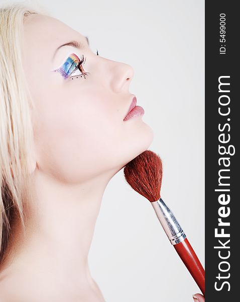 Beautiful girl with bright make-up, looks through a shoulder and holds a brush in a hand. Beautiful girl with bright make-up, looks through a shoulder and holds a brush in a hand